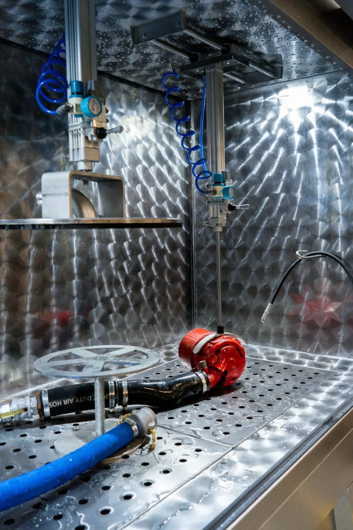 Inside a METClean cabinet: the perforated loading floor, a connected component, the wash hose and the overhead clamps