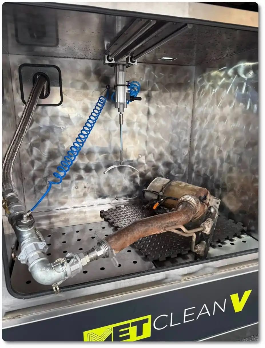 Inside a METClean V cabinet, with a DPF and its pipe connected to the wash hose on the floor