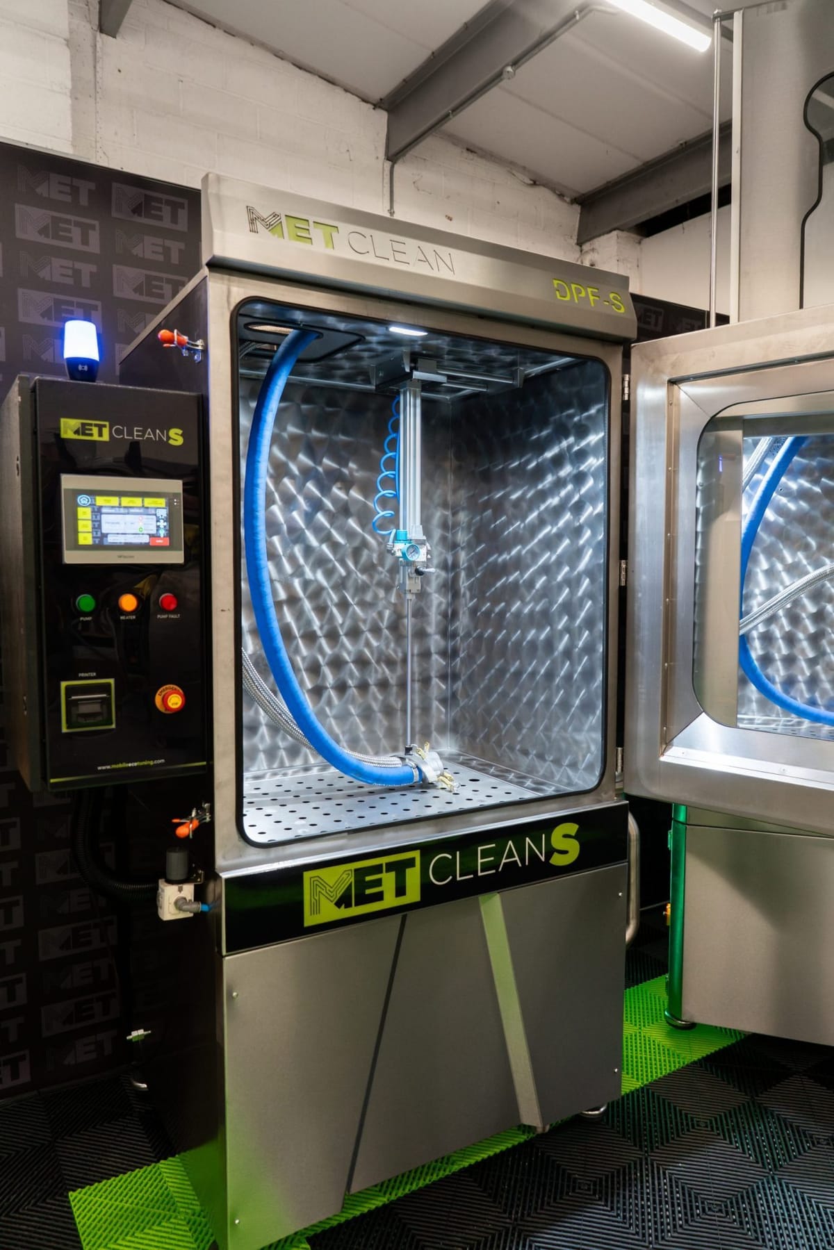 METClean S in a workshop with its door open, showing the stainless chamber and wash hose